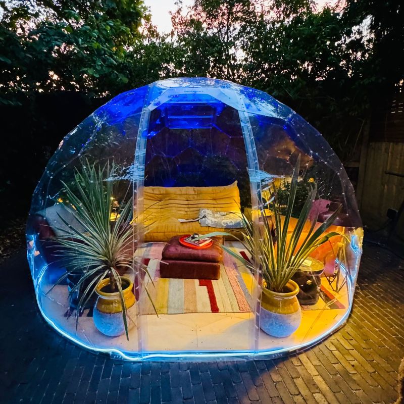 A GeoDomeX dome filled with plants, cushions and rugs, lit at night